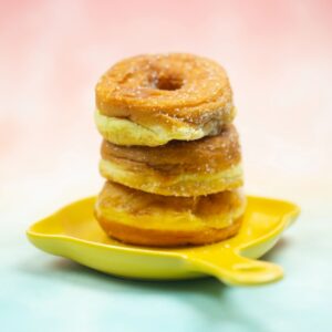 Three of ring donut with sugar glaze stacked up on yellow dish