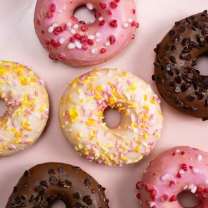 Lots of little donuts with white, pink and chocolate glaze on a pink background, top view
