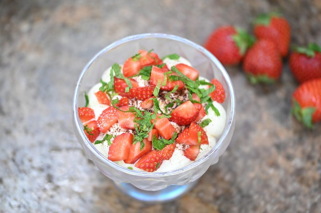 Close-up of strawberry tiramisu served in a glass bowl with fresh strawberries, mint, and creamy layers. Elegant seasonal dessert with soft blurred background, perfect for summer menus, gourmet sweets, and food photography concepts.