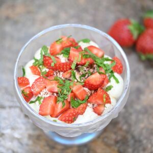 Close-up of strawberry tiramisu served in a glass bowl with fresh strawberries, mint, and creamy layers. Elegant seasonal dessert with soft blurred background, perfect for summer menus, gourmet sweets, and food photography concepts.